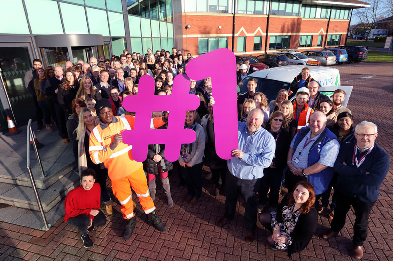 Group photo of Anglian Water employees outside Huntingdon office holding large Number One sign