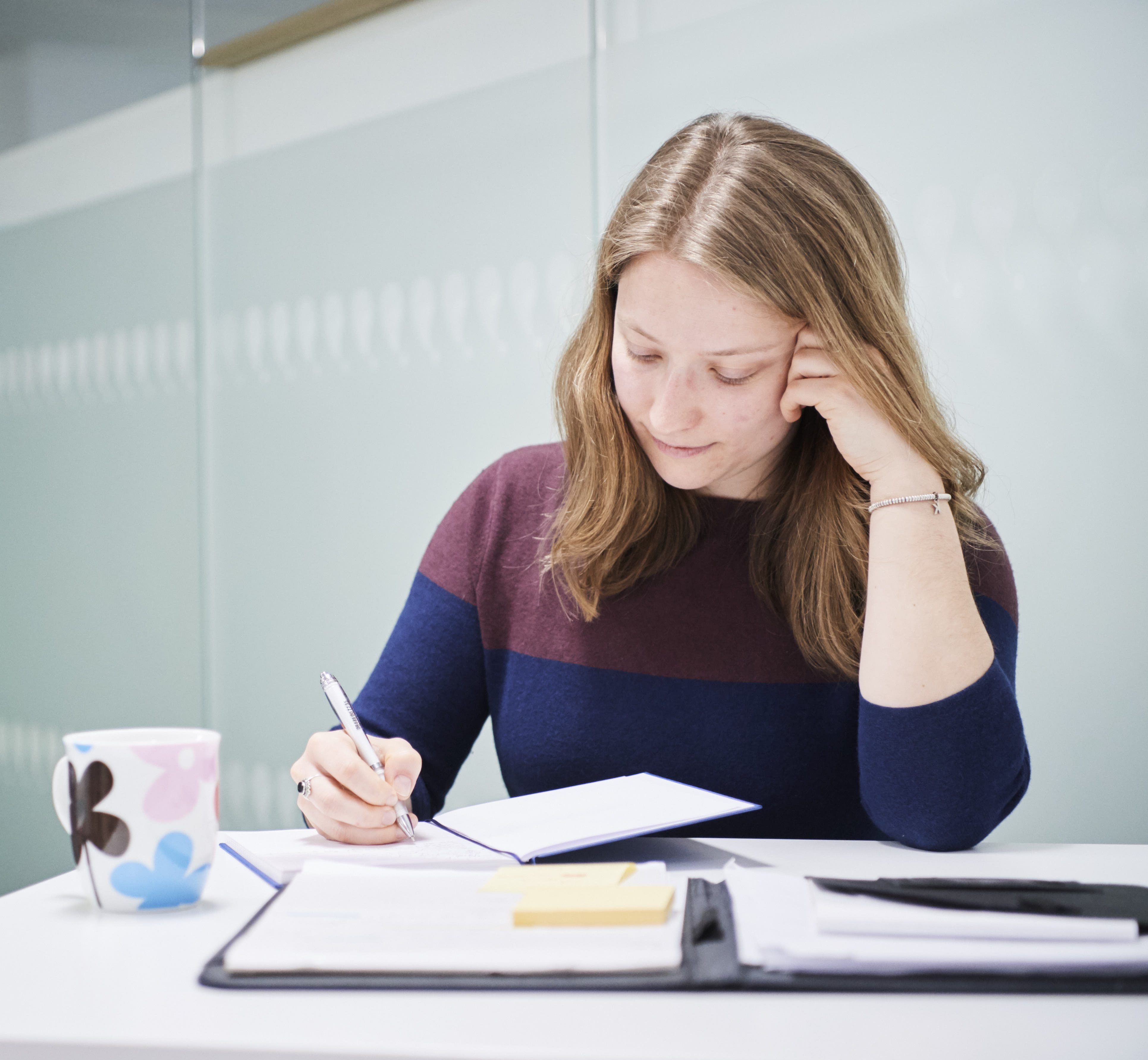 Female sitting a high desk in office environment writing in a notebook