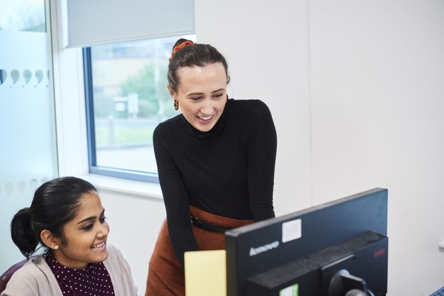 Two female co-workers in office environment looking at computer screen