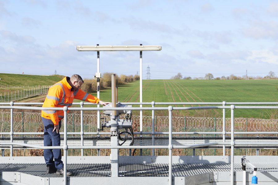 Man in high vis jacket checking equipment on a metal walkway atop a treatment facility